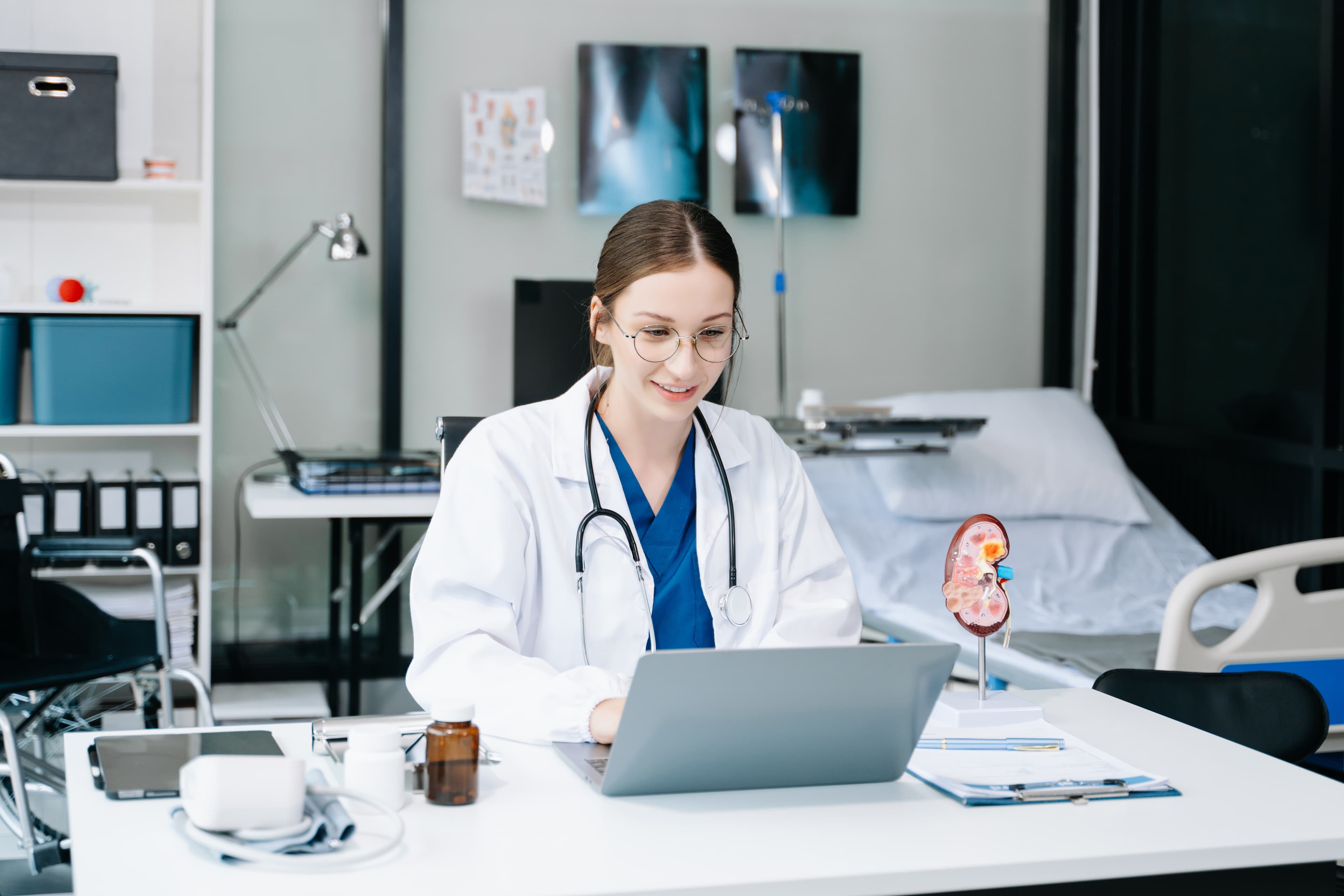 Healthcare professional working on a laptop in a clinical setting.